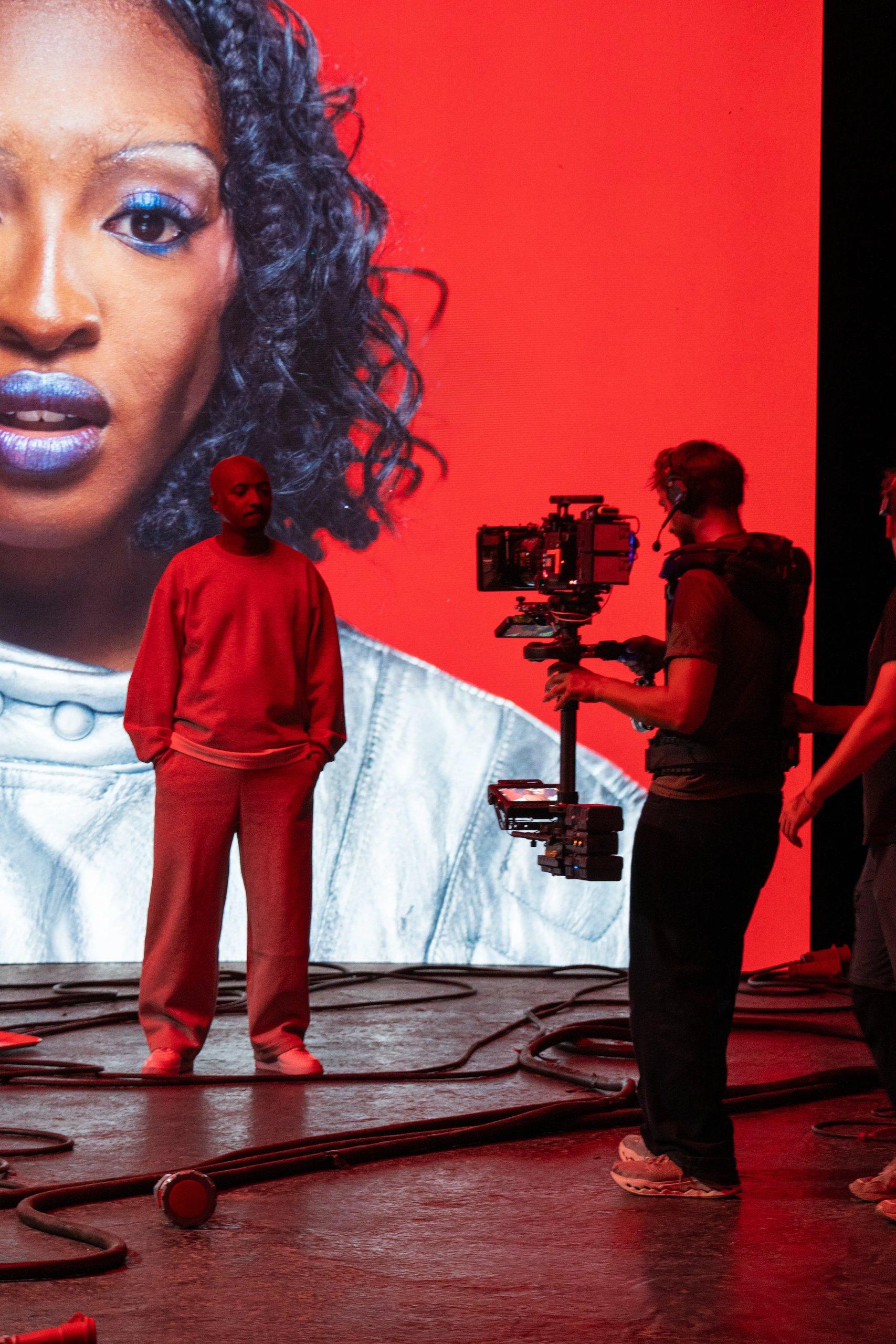 Opérateur Steadicam face à un artiste en survêtement, devant le portrait géant de la chanteuse sur fond rouge affiché sur le mur LED